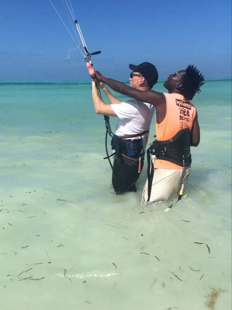 A Mawimbi teacher shows a guest how to hold the control bar, both standing waist-deep in the turquoise lagoon
